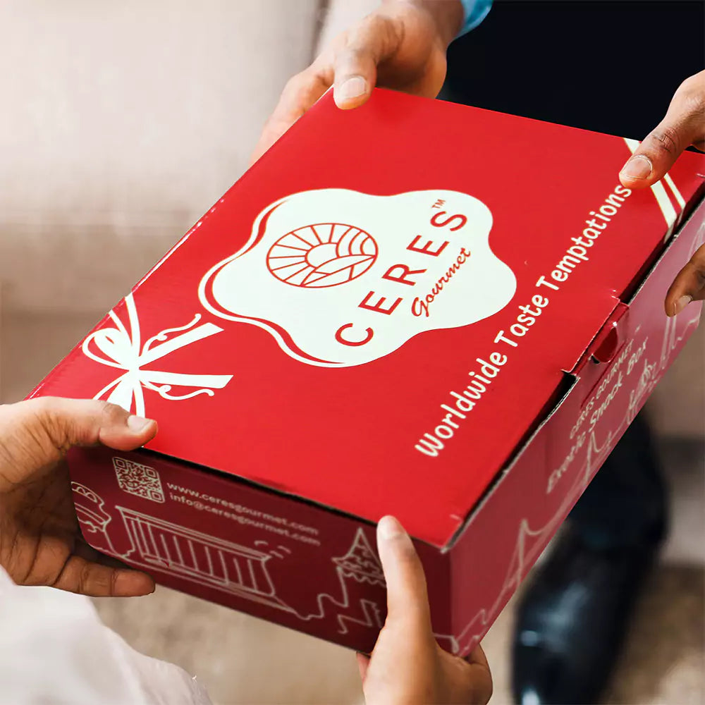 Two people exchange a Ceres Gourmet 50-Pack International Snack Box - Assorted Treats, featuring Worldwide Taste Temptations and white graphics—an ideal choice for employee appreciation or corporate gifting.