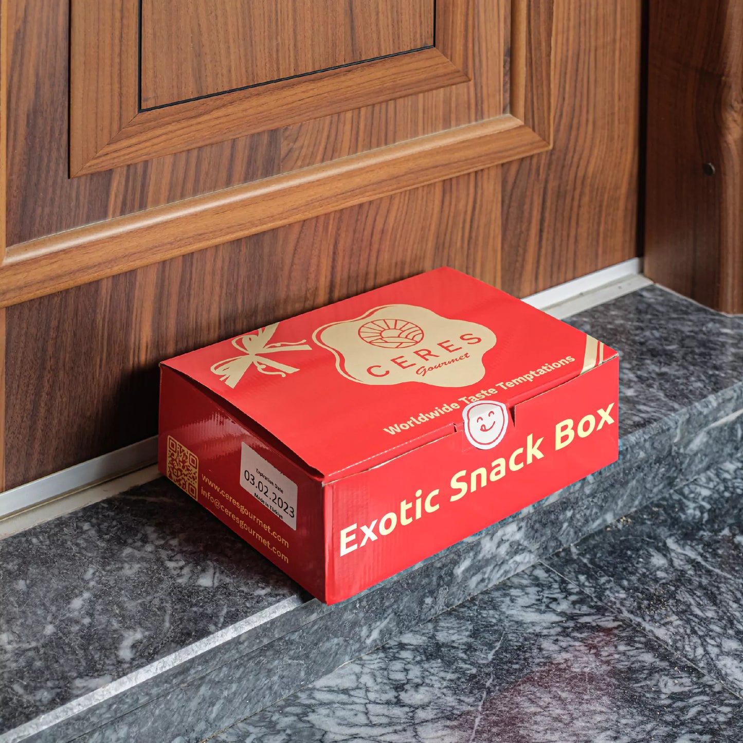 A 50-Pack International Snack Box - Assorted Treats by Ceres Gourmet rests on a marble doorstep, ideal for employee appreciation or corporate gifting.