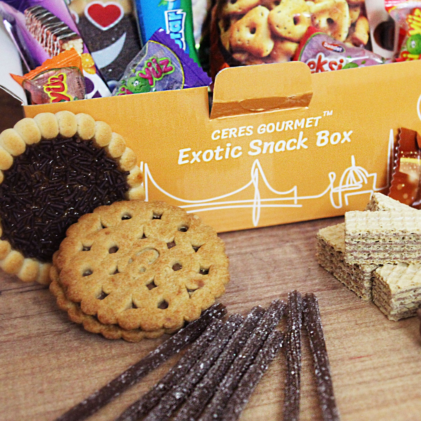 The Ceres Gourmet International Exotic Treats Box showcases 15 premium foreign rare snacks, including round cookies, wafer biscuits, chocolate sprinkles, fruit gummies, and candy sticks—all displayed on a wooden surface.