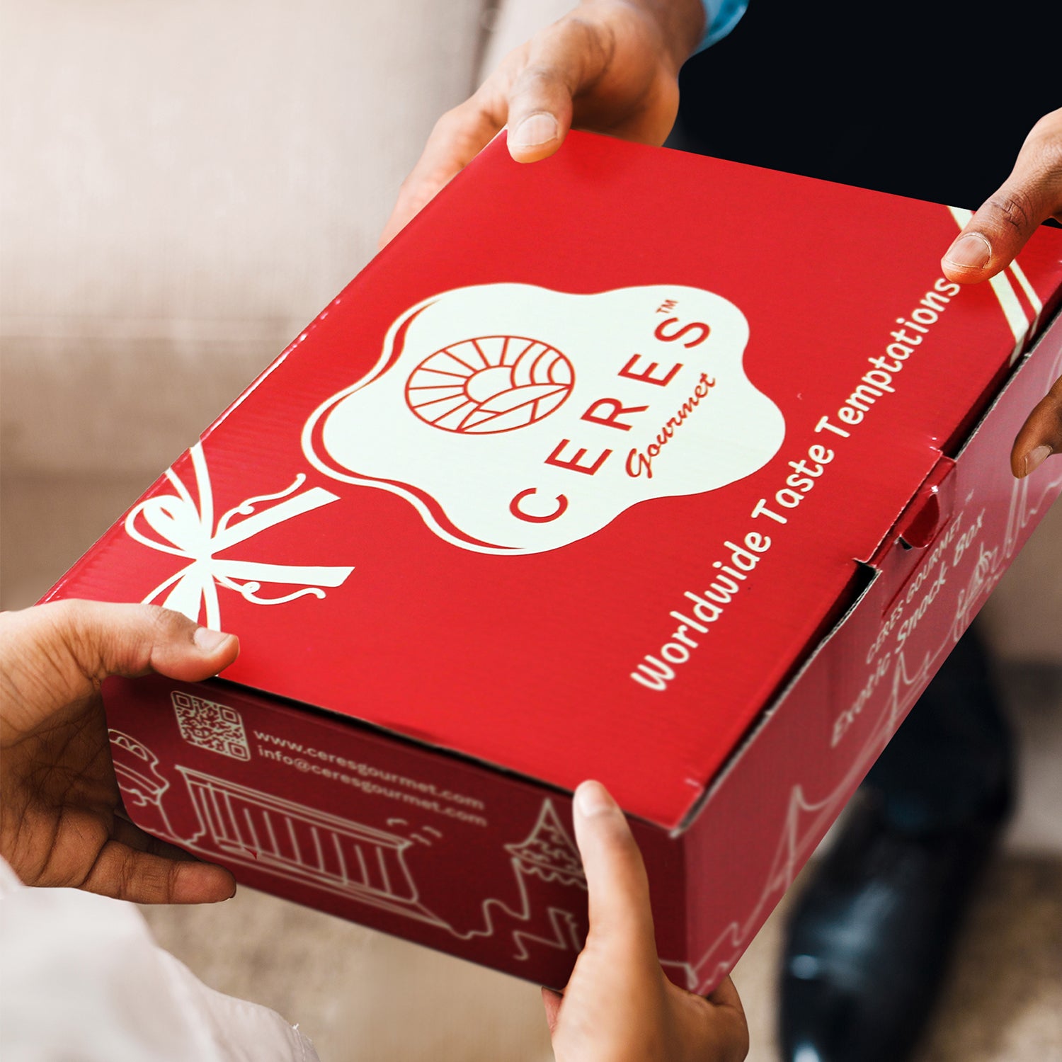 Two people exchange a red Ceres Gourmet International Snack Box (30 Unique Pcs) with âWorldwide Taste Temptationsâ printed on it, highlighting a gift or delivery of global snacks.