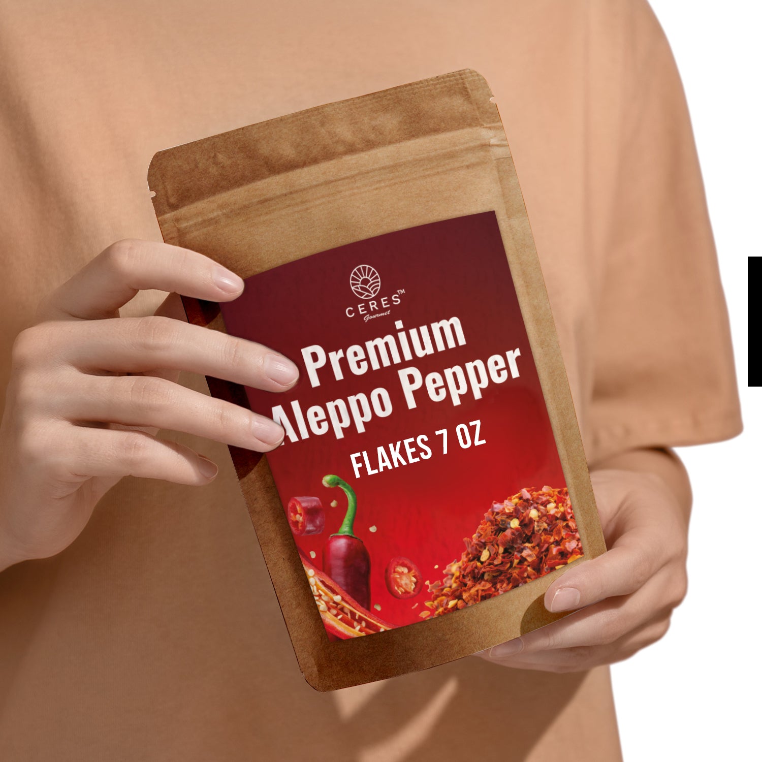 A person in a beige shirt holds a brown resealable pouch labeled Ceres Gourmet Premium Aleppo Pepper 7 Oz, Freshly Ground, featuring vibrant red pepper flakes and whole peppers on the packaging for exquisite flavor and mild heat.