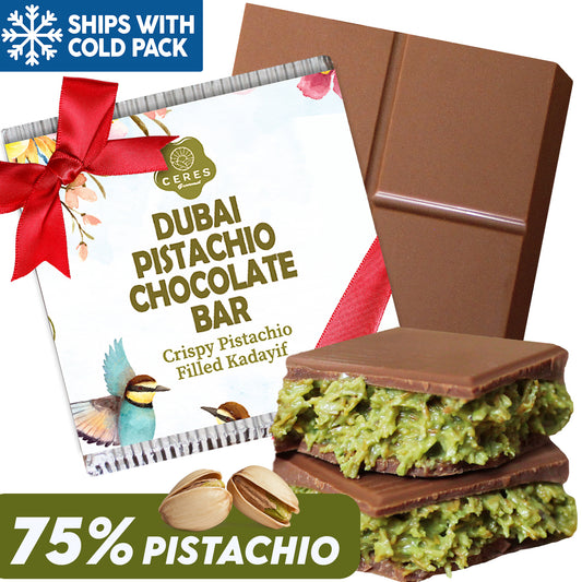 The Ceres Gourmet Dubai Chocolate Pistachio Bar 3.5 Oz Square, a luxury chocolate with 75% pistachio and green filling, is shown partially unwrapped. The packaging features a red bow and birds. Ships with cold pack.
