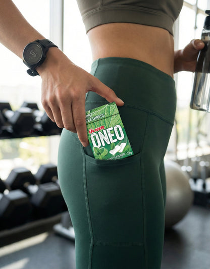 Person in green leggings with a Oneo package in a pocket, gym equipment in the background