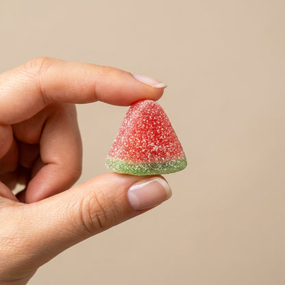 Hand holding a watermelon-flavored gummy candy against a beige background