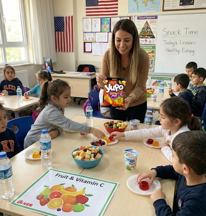 Teacher and students in a classroom setting with snacks and educational materials.