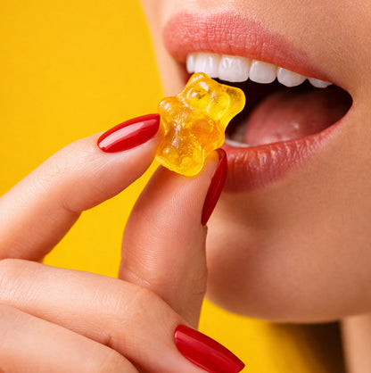 Close-up of a woman's mouth with a yellow gummy bear, against a bright yellow background
