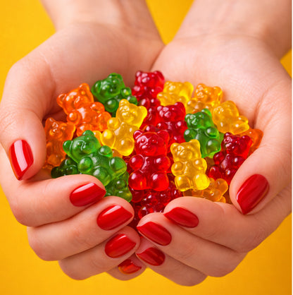 Colorful gummy bears held in hands with red nail polish against a yellow background