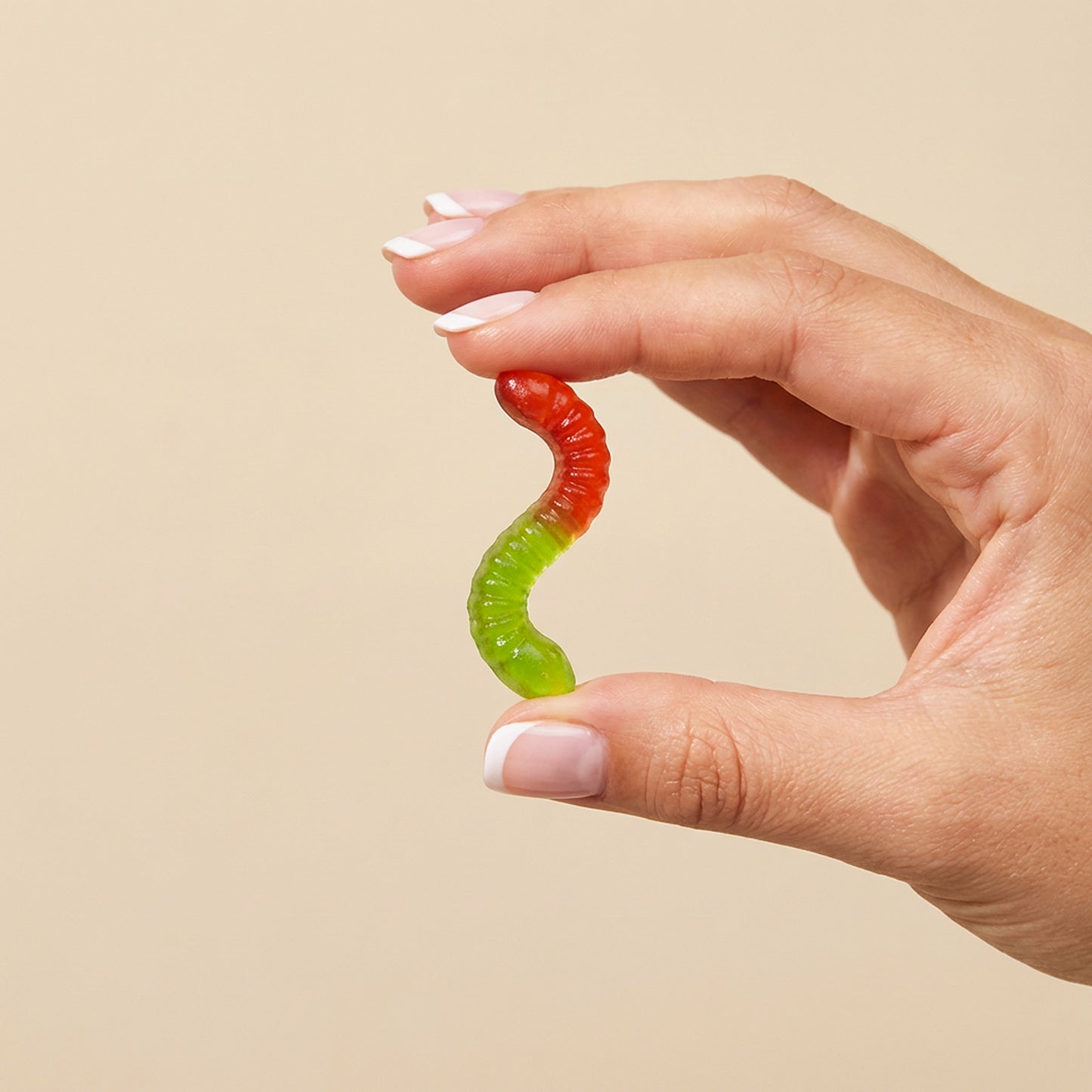 Hand holding a colorful gummy worm against a beige background