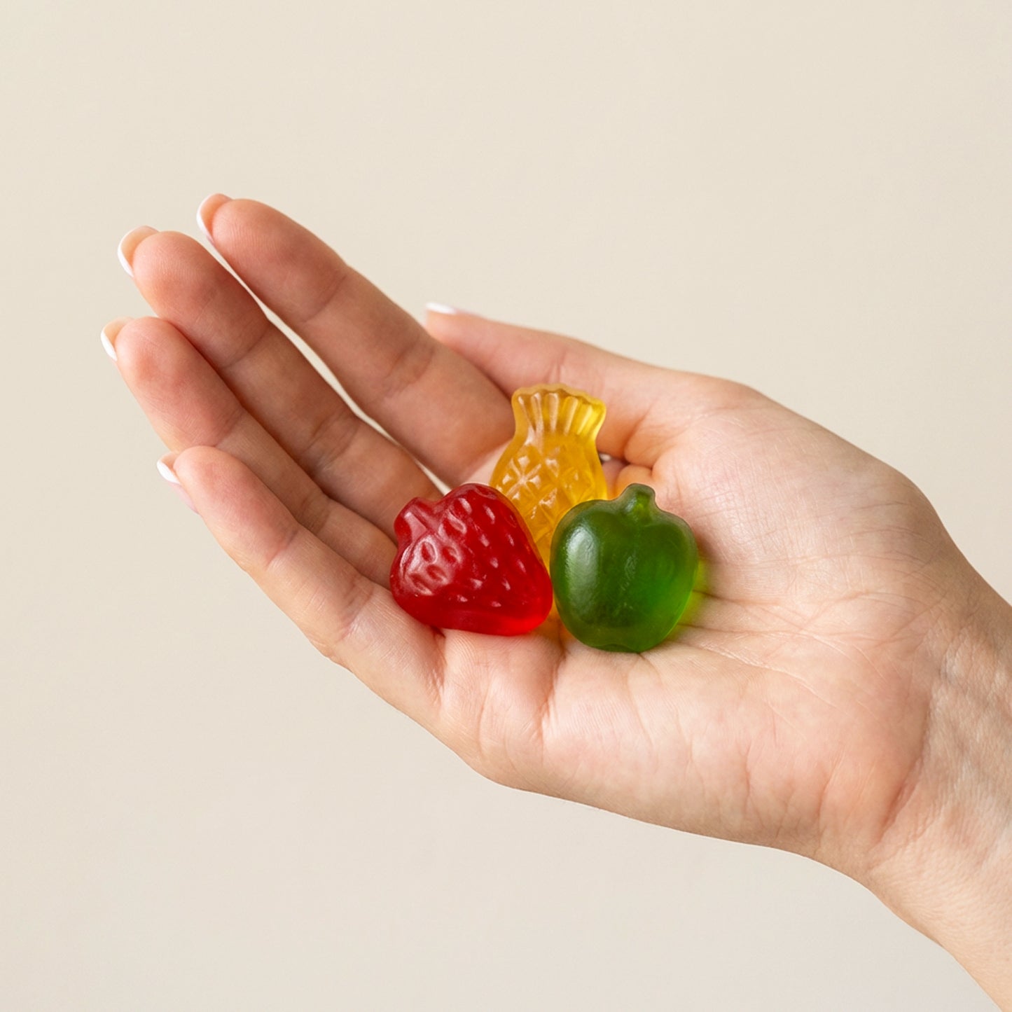 Hand holding three colorful gummy candies against a beige background