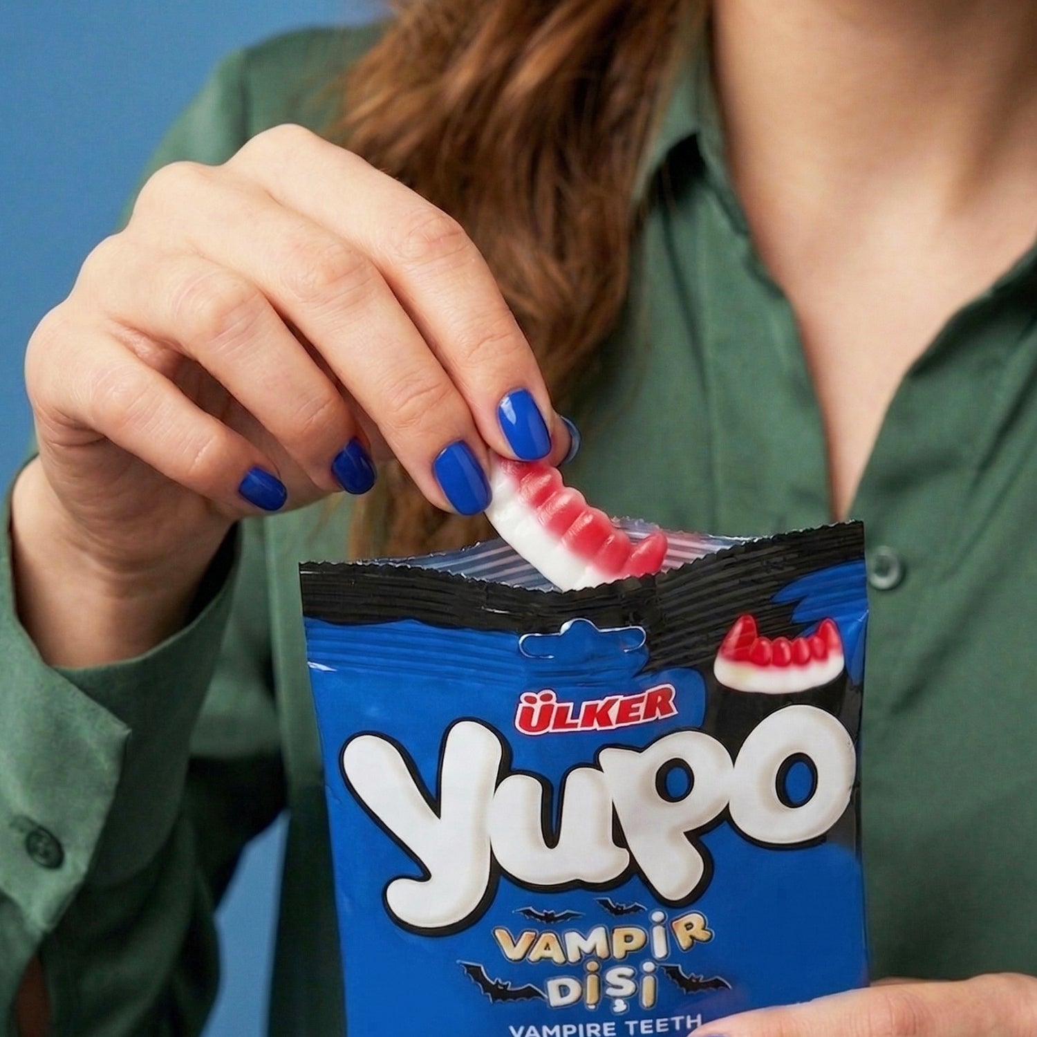 Person taking vampire teeth candy from a Yupo bag with blue packaging.