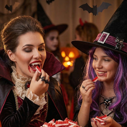Two women in Halloween costumes, one as a vampire and the other as a witch, enjoying Halloween treats.