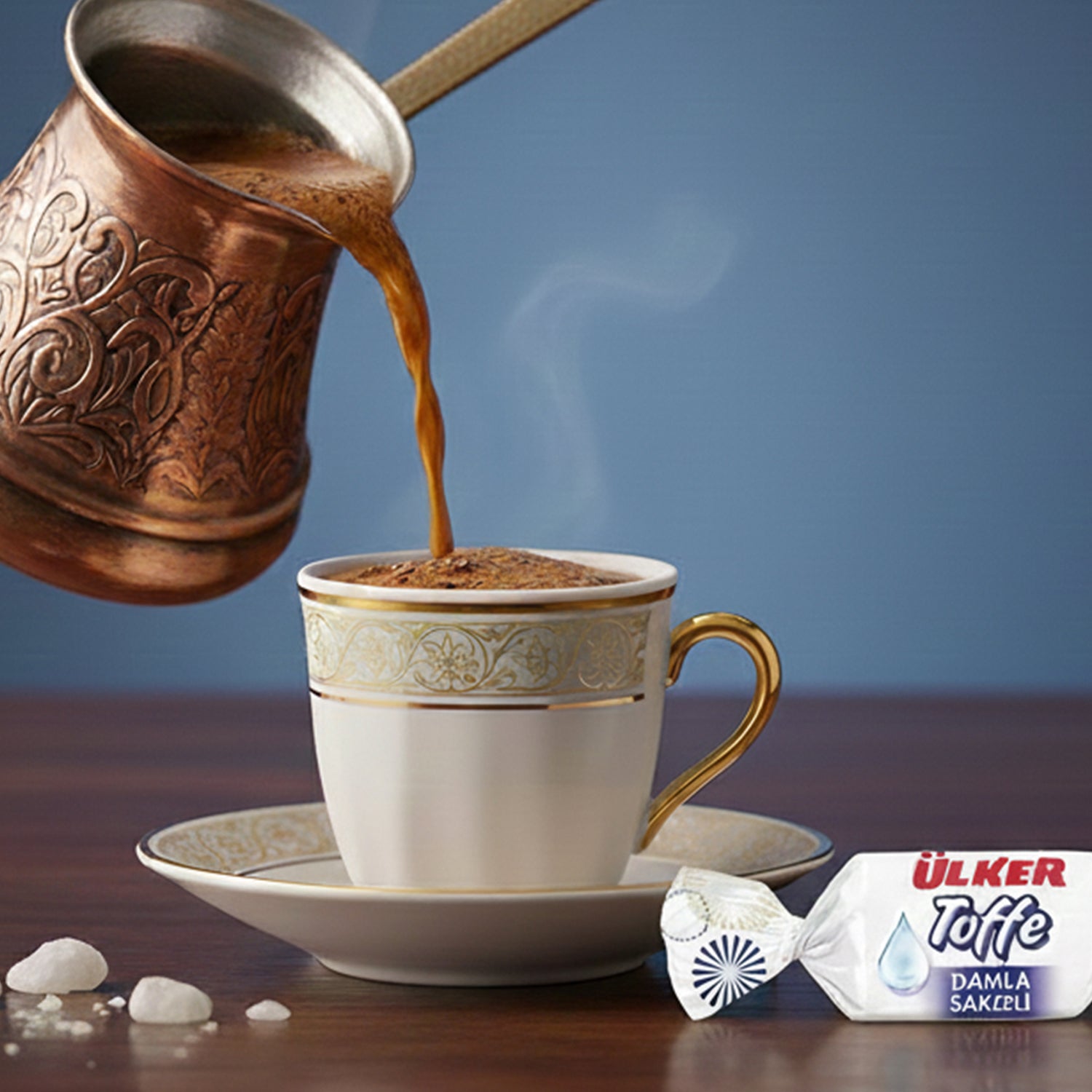 Cup of steaming coffee being poured from a bronze pot with a blue background, featuring Ulker Taffe package.