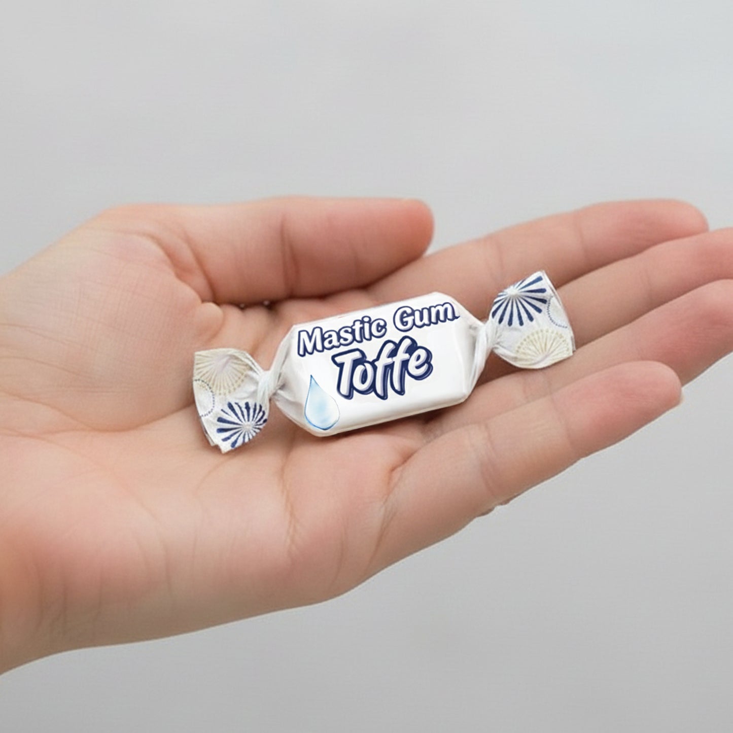 Hand holding two pieces of Mastice Gum Toffe candy against a gray background