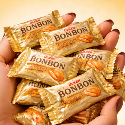 Hands holding multiple Ulker Bonbon caramel filled candy bars against a yellow background