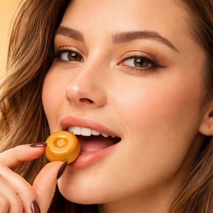 Woman holding a caramel candy close to her mouth against a beige background