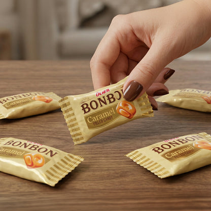 Hand holding a Bonbon Caramel candy wrapper on a wooden table with other candy wrappers.