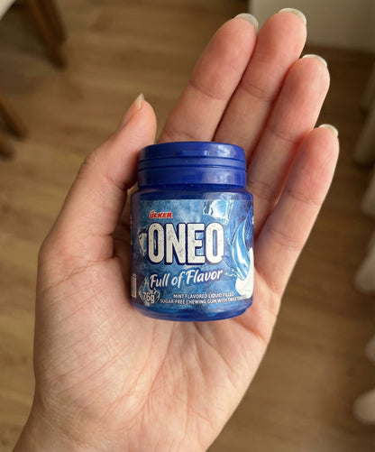 Hand holding a small container of Oneo mint-flavored liquid gum with a blue lid.