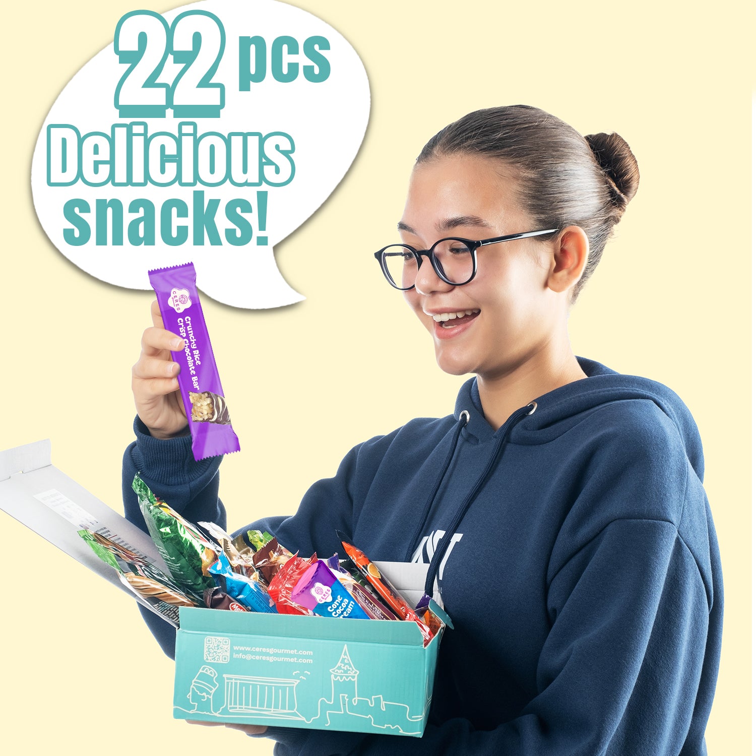 A smiling person in glasses and a blue hoodie holds an open Ceres Gourmet 50-Pack Snack Boxes from Around the World, excitedly looking at a purple snack bar. A speech bubble says, 50 pcs Delicious snacks! 