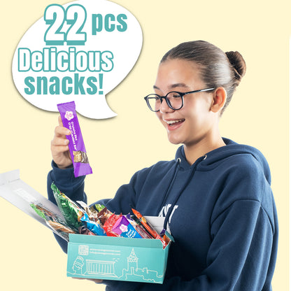 A smiling person in glasses and a blue hoodie holds an open Ceres Gourmet 50-Pack Snack Boxes from Around the World, excitedly looking at a purple snack bar. A speech bubble says, 50 pcs Delicious snacks! 