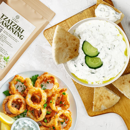 A bowl of Greek Tzatziki Dip, garnished with cucumber and olive oil, is served with pita bread. Beside it is fried calamari with lemon, parsley, and a packet of Ceres Gourmet Authentic Greek Tzatziki Dip Spice Blend 4 oz.
