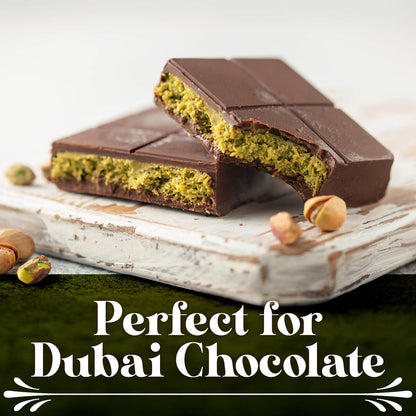 Two chocolates with green pistachio filling rest on a rustic white wooden board, surrounded by pistachios and Ceres Gourmet Baked & Chopped Kataifi 11-22-44 lb. Perfect for Dubai chocolate gourmet desserts.