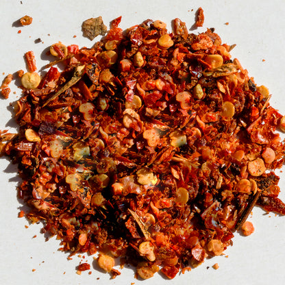 A close-up of Ceres Gourmet Dried Tomato Powder (5.3 oz, 100% pure), scattered on a white surface with seeds and dried red chili flakes—perfect for sauces, soups, paste, and more.