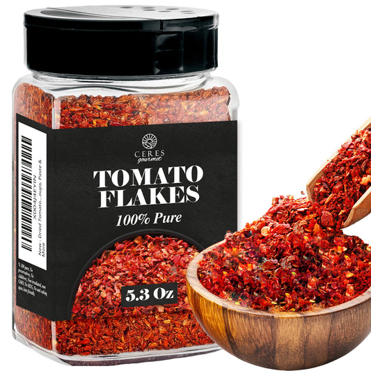 A clear jar of Ceres Gourmet Dried Tomato Powder – 5.3 oz, 100% pure, sits beside a wooden spoon filled with vibrant red powder. This non-GMO product is perfect for sauces, soups, paste, and adding rich tomato flavor to your recipes.