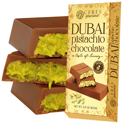 A stack of chocolate bars with green pistachio filling sits next to a Ceres Gourmet box labeled "Dubai Chocolate Bar Pistachio with Milky Chocolate and Knafeh," featuring images of the bar and pistachios.