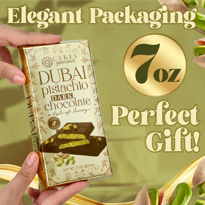 A hand holds a gold-wrapped Ceres Gourmet Dark Chocolate Dubai Crispy Knafeh Pistachio Bar (7oz) against a green backdrop with pistachios, showcasing elegant packaging—a perfect gourmet gift! Indulge in pistachio cream-filled dark chocolate.