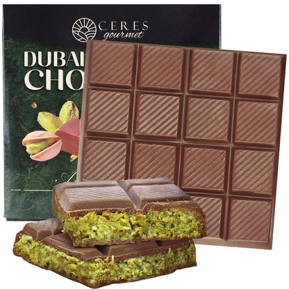 A Ceres Gourmet Dubai Chocolate Pistachio Bar (Mlky Chocolate & Crispy Knafeh – 3.5oz) with a checkered pattern is shown, two pieces broken to reveal green pistachio filling, alongside its branded packaging.