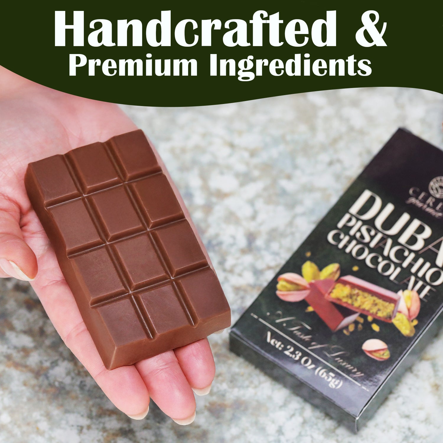 A hand holds a rectangular Ceres Gourmet Dubai Chocolate Bar (2.3 oz, 65g) beside its packaging on a marble surface. The box displays “Dubai Chocolate Bar” and above reads, “Handcrafted & Premium Ingredients.” Available in 3-12-24 Packs.