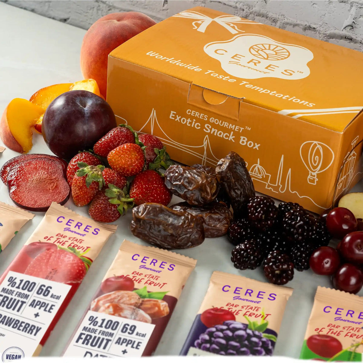 A CERES Gourmet Exotic Snack Box is placed behind fresh plums, strawberries, blackberries, grapes, dates, and peaches, with several Ceres Gourmet Fruit Strips Variety Pack vegan gluten-free snack bars displayed in front.