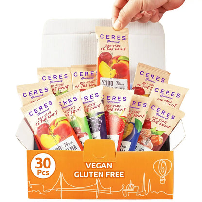 A hand holds a Ceres Gourmet Fruit Strips Variety Pack bar above an open orange box of 30 vegan, gluten-free bars. Each Ceres Gourmet bar features colorful fruit images and contains no added sugar for a naturally sweet snack.