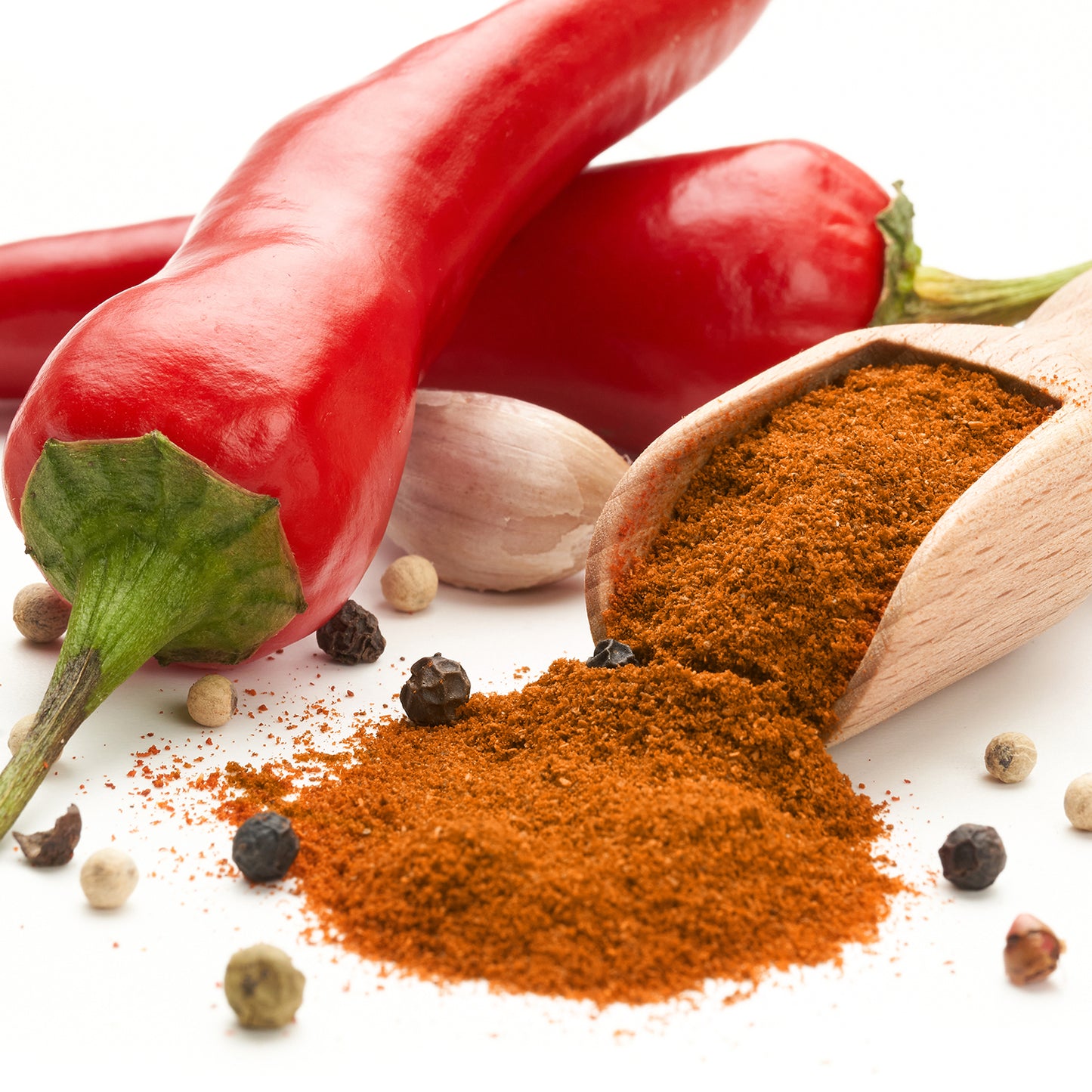 Whole red chilies, garlic cloves, and peppercorns surround a wooden scoop spilling Ceres Gourmet Harissa Seasoning Blend, 3.5 oz—an aromatic and mildly spicy North African powder—onto a white surface.