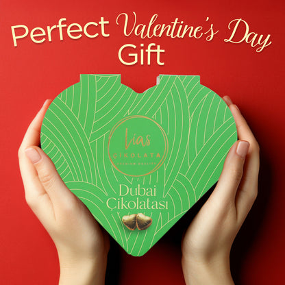 Hands holding a green, heart-shaped box of “Love Bite Dubai Chocolate Pistachio, 10 Bite-Size Pieces” by Ceres Gourmet against a red background, with “Perfect Valentine’s Day Gift” at the top.