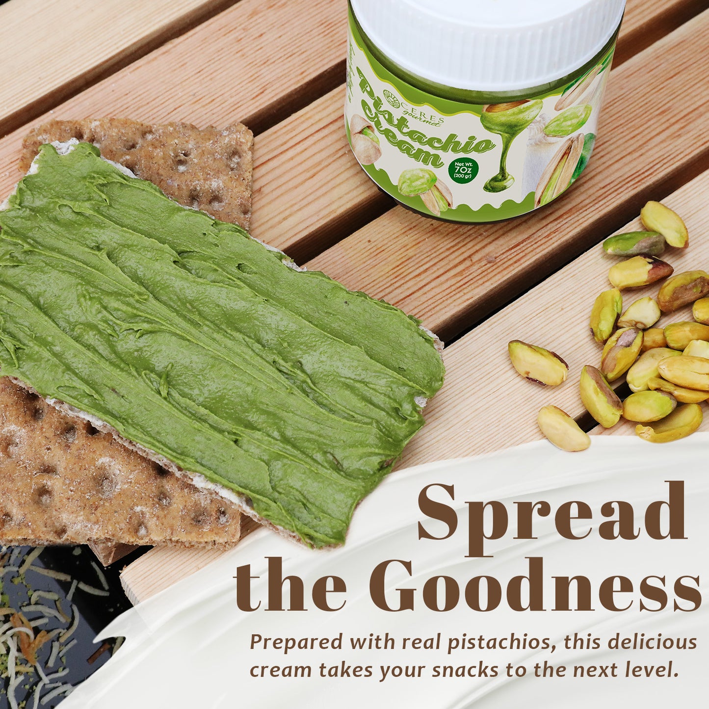 Pistachio cream spread on a cracker with pistachios on a wooden surface, featuring a container of the product.