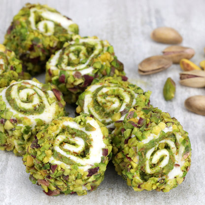 Ceres Gourmet’s Turkish Delight with Dubai Chocolate Filling (17.6 oz) features round, swirl-shaped sweets with a pistachio coating, arranged alongside whole and shelled pistachios on a light surface.