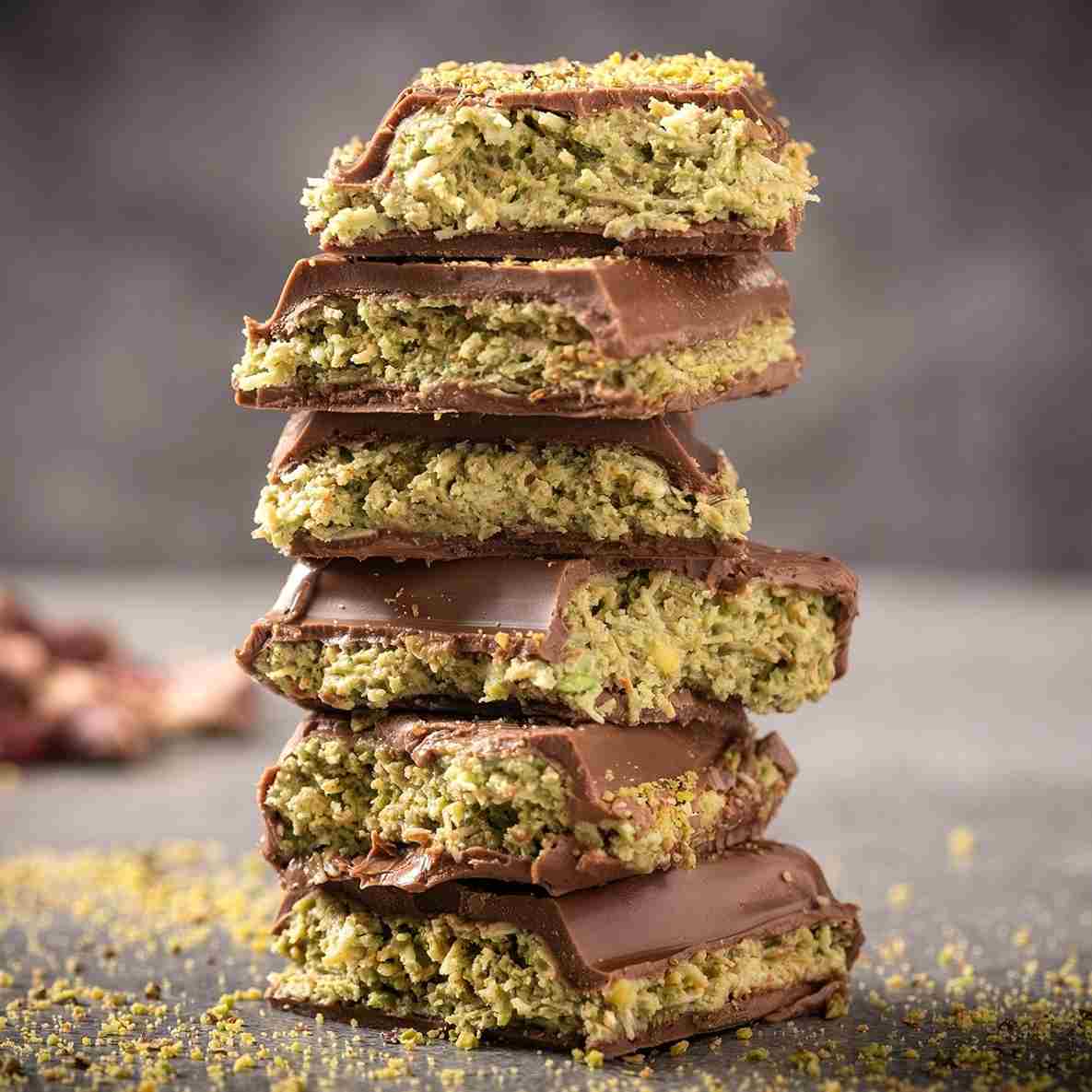 A stack of Ceres Gourmet Viral Halloween Dubai Chocolate Bars, 75% Pistachio, featuring a rich pistachio cream filling and chocolate coating, is displayed on a grey surface with a blurred background.