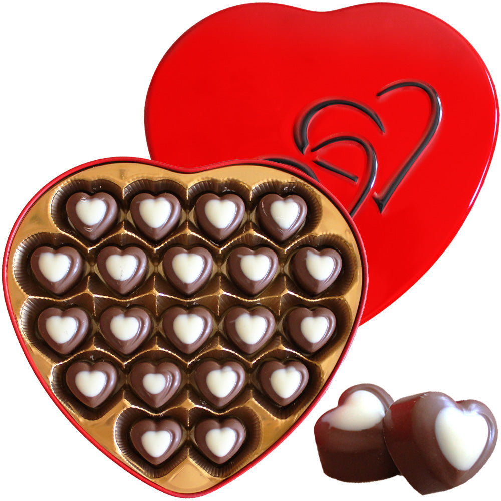 A red, heart-shaped box filled with heart-shaped chocolates topped with white centers. The lid, also heart-shaped, is beside the box and features an embossed heart design. Two chocolates are placed in front.